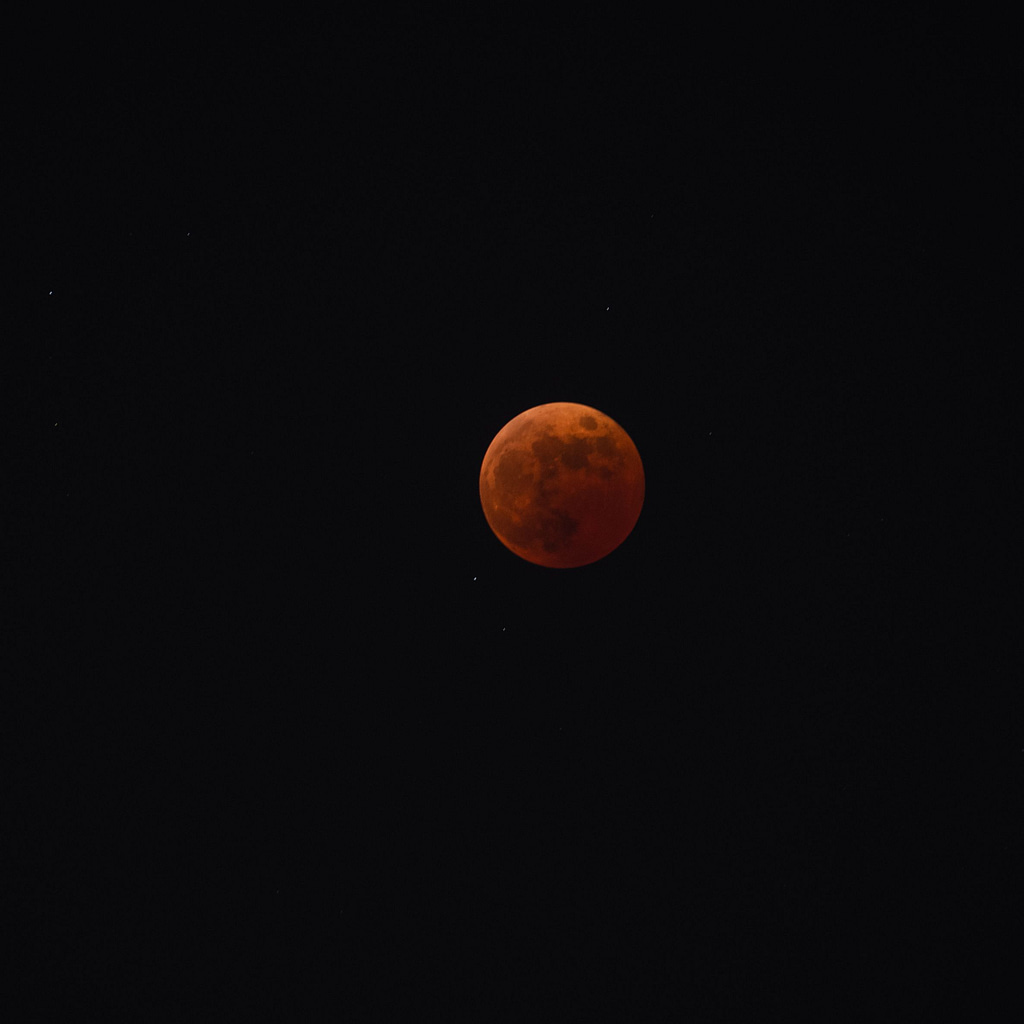 Full moon in Pisces during a lunar eclipse glowing orange against a dark night sky