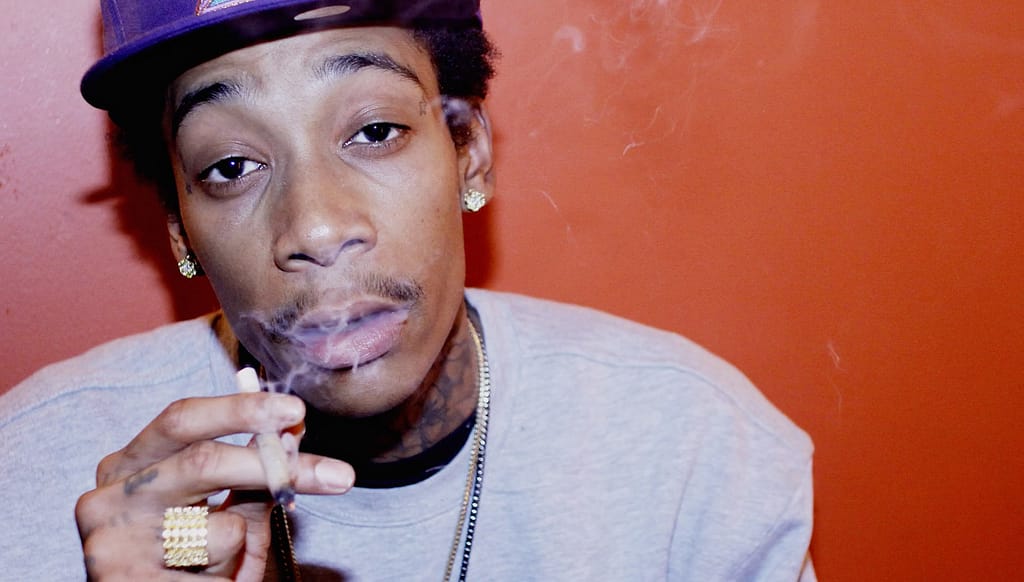 Wiz Khalifa smoking looking stoned in front of red wall