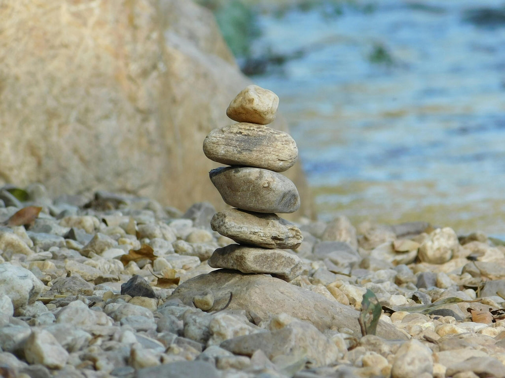 Rocks pile ritual symbolizing sacred secularism, with a river in the background - nature as a sacred refuge for the spiritual atheist seeker