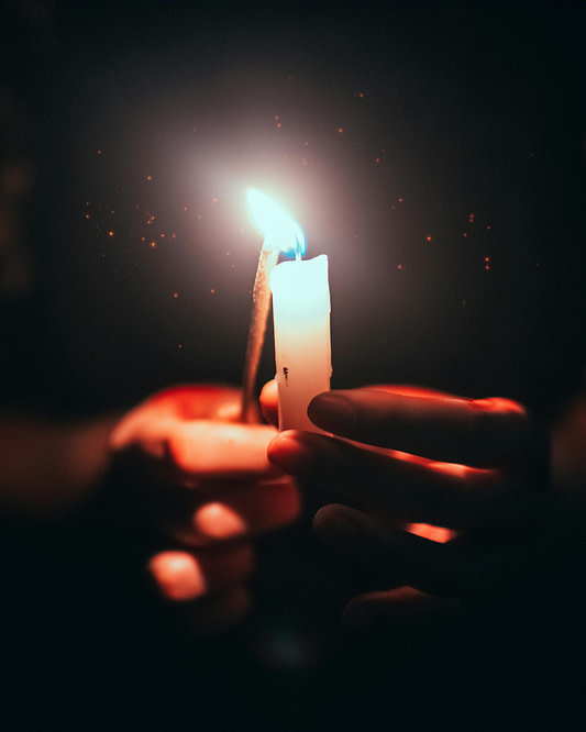Hands lighting a small candle flame in the dark symbolizing creative spark and inspiration